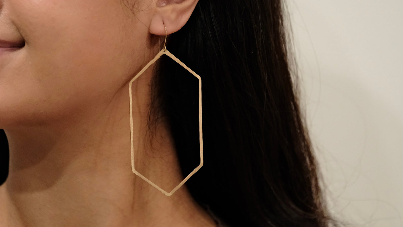Close-up of a woman wearing gold hexagonal earrings with a neutral background